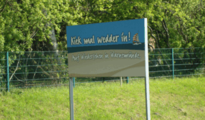 Ein Ortsasugangsschild in Warnemünde. Oben steht "Kiek mal wedder in!", darunter "Auf Wiedersehen in Warnemünde."